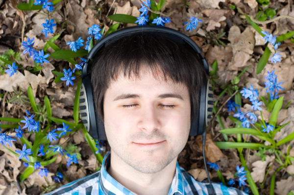 A man laying in flowers, eyes closed with headphones on