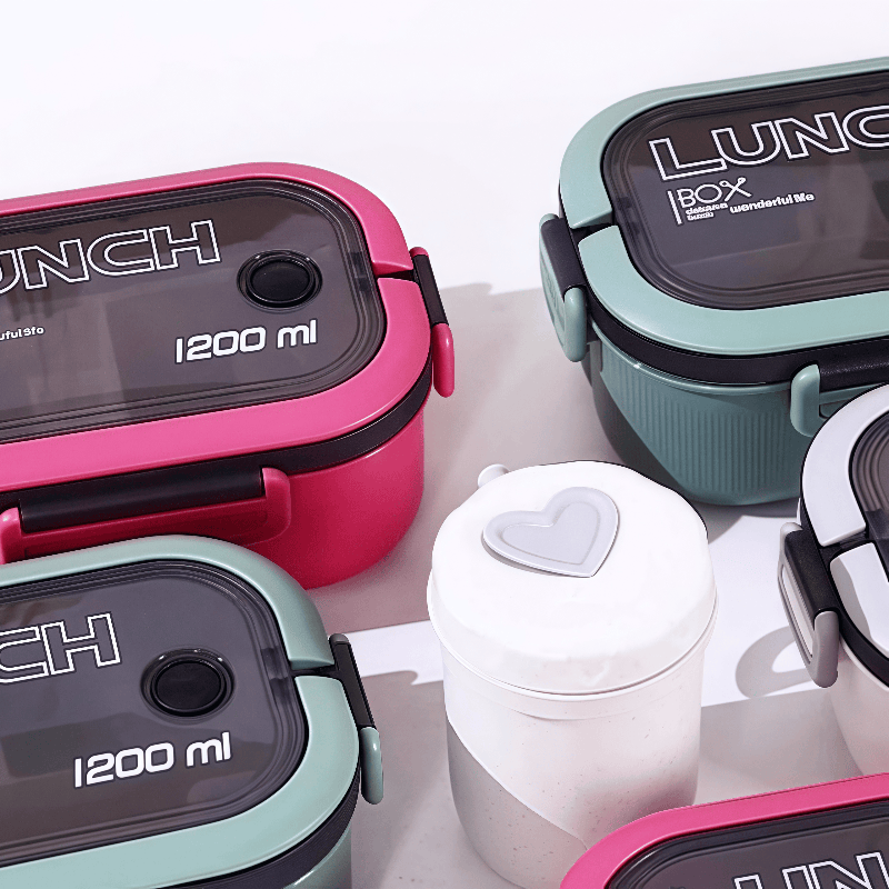 Various colored lunch boxes on a white table with a white tumbler centered between them