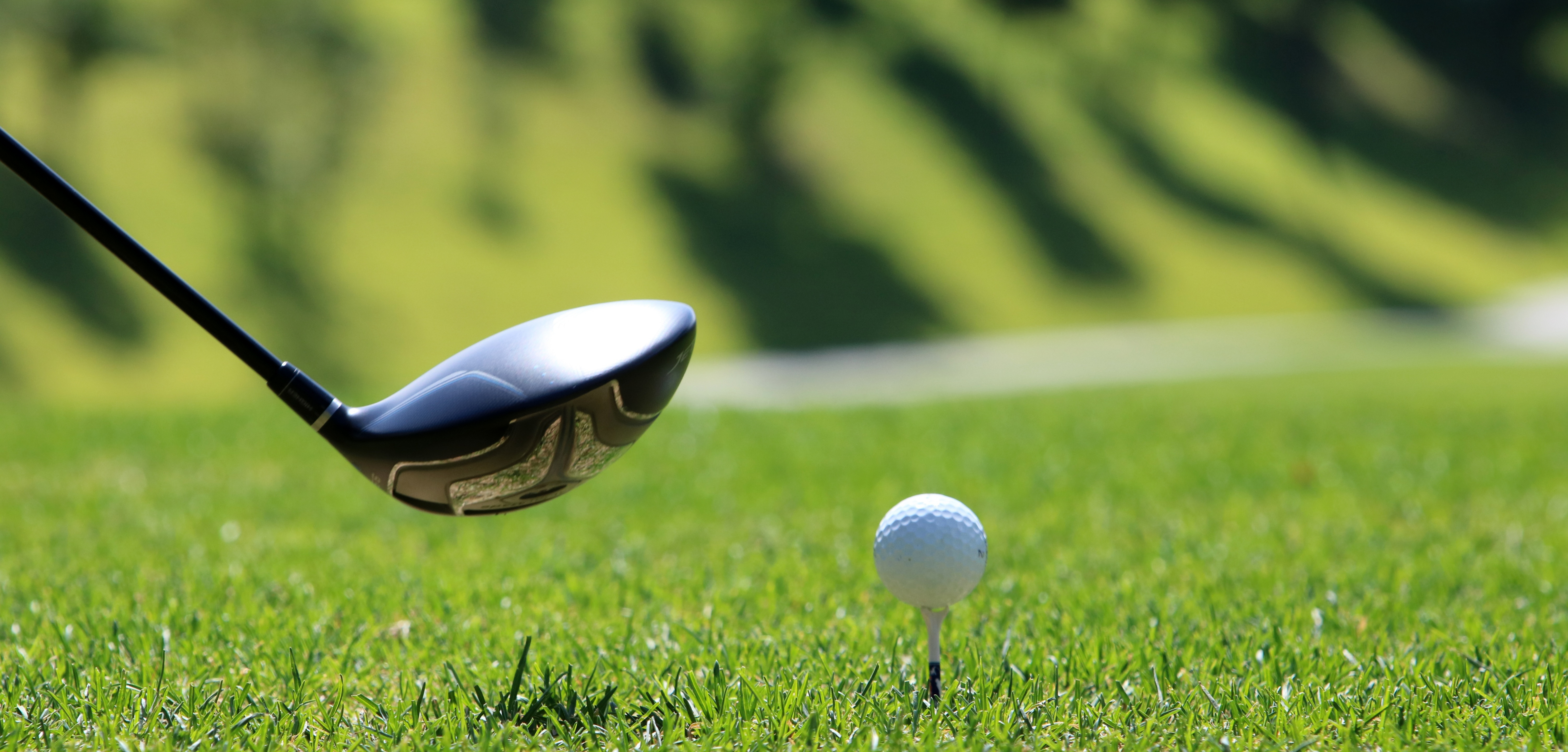 Golf ball placed on green grass with a golf club on the left 